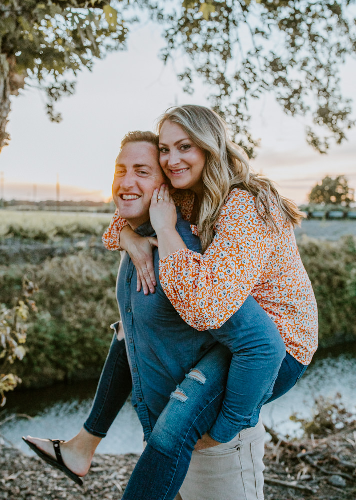 Sacramento River Engagement Session Northern California Weiner dog engagement shoot outfit inspo engagement photos with dog couples shoot posing golden hour sacramento river rachel christopherson photography piggy back ride smile
