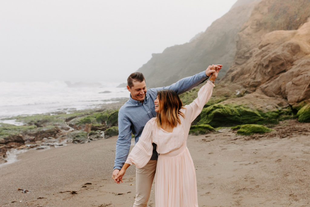 couple look at each other on beach in airplane pose, Marin Headlands Engagement Photos, Bay Area Engagement Photos, Bay Area Engagement Photo Locations, Engagement Photo Outfits, Bay Area Beach Engagement Photos, Dog Friendly Bay Area Beaches, Best Locations for Bay Area Engagement Photos, San Francisco Engagement Photos, What to Wear for Engagement Photos, Engagement Photos with dogs, Rachel Christopherson Photography LLC