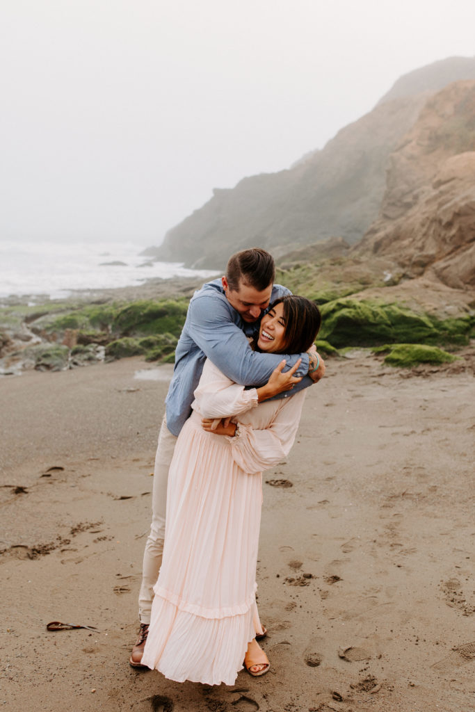 man hugging woman on beach, Marin Headlands Engagement Photos, Bay Area Engagement Photos, Bay Area Engagement Photo Locations, Engagement Photo Outfits, Bay Area Beach Engagement Photos, Dog Friendly Bay Area Beaches, Best Locations for Bay Area Engagement Photos, San Francisco Engagement Photos, What to Wear for Engagement Photos, Engagement Photos with dogs, Rachel Christopherson Photography LLC