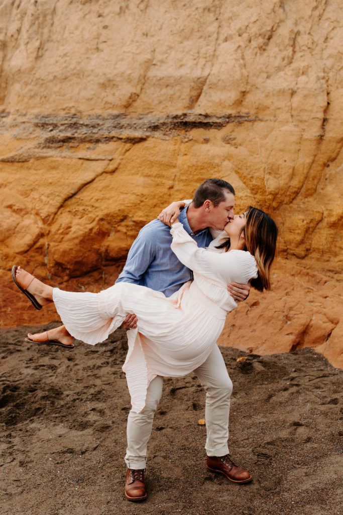 man cradling woman while kissing, Marin Headlands Engagement Photos, Bay Area Engagement Photos, Bay Area Engagement Photo Locations, Engagement Photo Outfits, Bay Area Beach Engagement Photos, Dog Friendly Bay Area Beaches, Best Locations for Bay Area Engagement Photos, San Francisco Engagement Photos, What to Wear for Engagement Photos, Engagement Photos with dogs, Rachel Christopherson Photography LLC