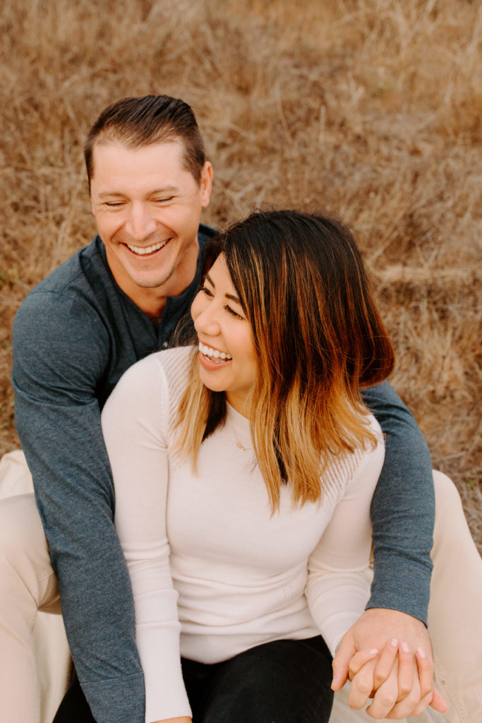 Couple sitting and laughing in grass, Marin Headlands Engagement Photos, Bay Area Engagement Photos, Bay Area Engagement Photo Locations, Engagement Photo Outfits, Coastal Bay Area Engagement Photos, Dog Friendly Bay Area Beaches, Best Locations for Bay Area Engagement Photos, San Francisco Engagement Photos, What to Wear for Engagement Photos, Engagement Photos with dogs, Rachel Christopherson Photography LLC