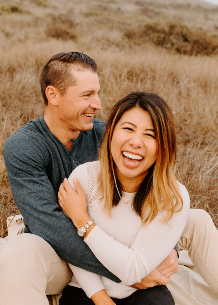 couple laughing together on grass, Marin Headlands Engagement Photos, Bay Area Engagement Photos, Bay Area Engagement Photo Locations, Engagement Photo Outfits, Coastal Bay Area Engagement Photos, Dog Friendly Bay Area Beaches, Best Locations for Bay Area Engagement Photos, San Francisco Engagement Photos, What to Wear for Engagement Photos, Engagement Photos with dogs, Rachel Christopherson Photography LLC
