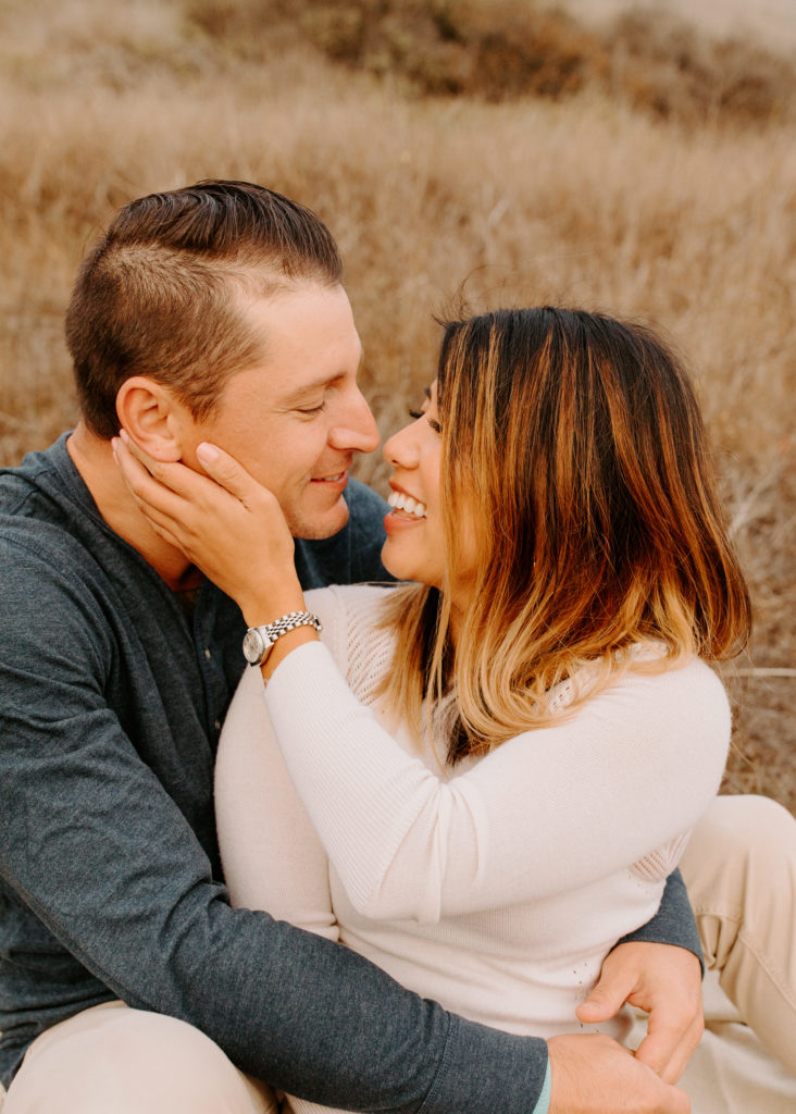 couple smiling at each other on grass, Marin Headlands Engagement Photos, Bay Area Engagement Photos, Bay Area Engagement Photo Locations, Engagement Photo Outfits, Coastal Bay Area Engagement Photos, Dog Friendly Bay Area Beaches, Best Locations for Bay Area Engagement Photos, San Francisco Engagement Photos, What to Wear for Engagement Photos, Engagement Photos with dogs, Rachel Christopherson Photography LLC