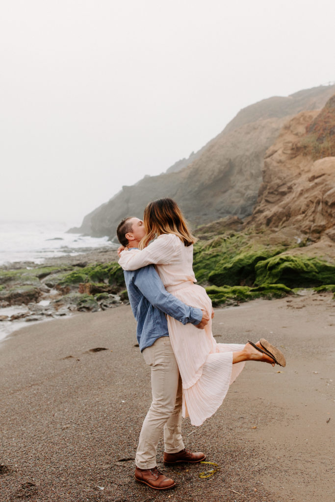 man lifting woman on beach for kiss, Marin Headlands Engagement Photos, Bay Area Engagement Photos, Bay Area Engagement Photo Locations, Engagement Photo Outfits, Bay Area Beach Engagement Photos, Dog Friendly Bay Area Beaches, Best Locations for Bay Area Engagement Photos, San Francisco Engagement Photos, What to Wear for Engagement Photos, Engagement Photos with dogs, Rachel Christopherson Photography LLC
