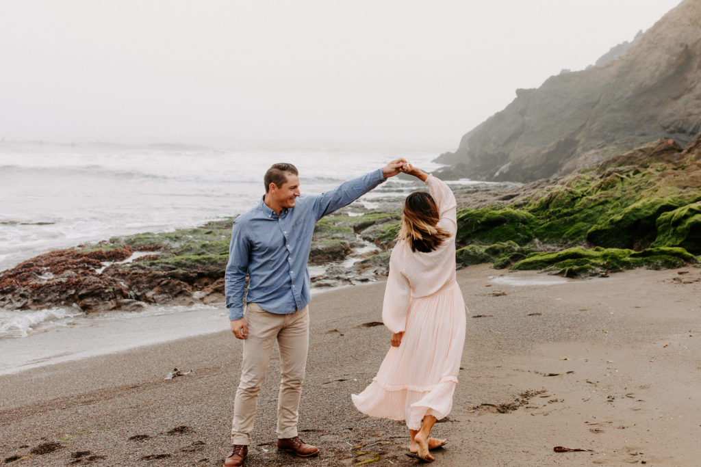 man spinning woman on SF beach, Marin Headlands Engagement Photos, Bay Area Engagement Photos, Bay Area Engagement Photo Locations, Engagement Photo Outfits, Bay Area Beach Engagement Photos, Dog Friendly Bay Area Beaches, Best Locations for Bay Area Engagement Photos, San Francisco Engagement Photos, What to Wear for Engagement Photos, Engagement Photos with dogs, Rachel Christopherson Photography LLC