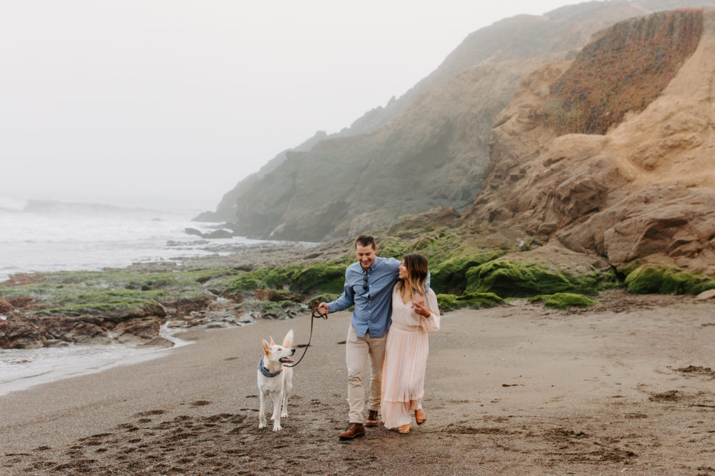 couple laughing while walking dog on beach, Marin Headlands Engagement Photos, Bay Area Engagement Photos, Bay Area Engagement Photo Locations, Engagement Photo Outfits, Bay Area Beach Engagement Photos, Dog Friendly Bay Area Beaches, Best Locations for Bay Area Engagement Photos, San Francisco Engagement Photos, What to Wear for Engagement Photos, Engagement Photos with dogs, Rachel Christopherson Photography LLC