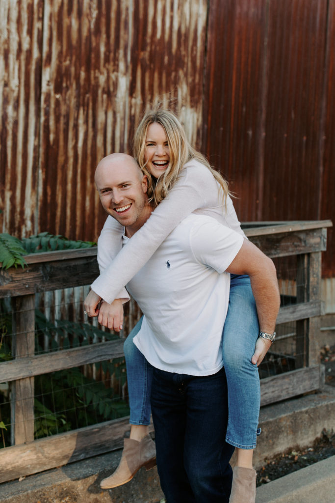 couple piggy back ride in front of rustic building, Sacramento engagement photos, sacramento engagement, sacramento engagement photographer sacramento engagement photo locations, sacramento wedding photographer, rachel christopherson photography, engagement photo outfit inspo