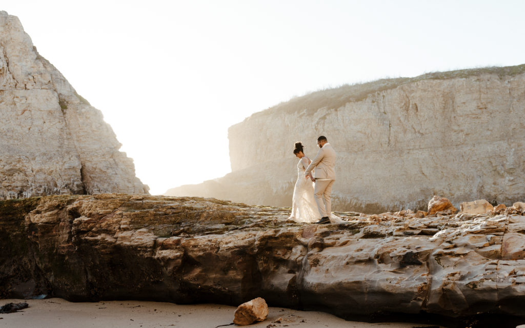 bride and groom walking on beach cliff, Santa cruz wedding, santa cruz elopement, santa cruz wedding photographer, santa cruz elopement photographer, big sur elopement, boho beach bride, california boho elopement, boho wedding dress, best places to elope in California, California elopement, California beach elopement, boho bride inspo, Rachel Christopherson Photography 