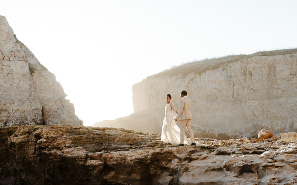 bride and groom walking on beach cliff, Santa cruz wedding, santa cruz elopement, santa cruz wedding photographer, santa cruz elopement photographer, big sur elopement, boho beach bride, california boho elopement, boho wedding dress, best places to elope in California, California elopement, California beach elopement, boho bride inspo, Rachel Christopherson Photograph