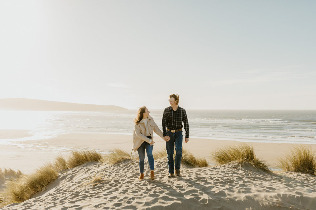 Rachel Christopherson Engagement Photographer-Engaged couple holding hands and smiling at each other on beach-San Francisco Engagement Photos, Northern California Engagement Photos, Point Reyes Engagement Photos, Bodega Bay Engagement Photos, Dillon Beach Engagement Photos, Bay Area Engagement Photos