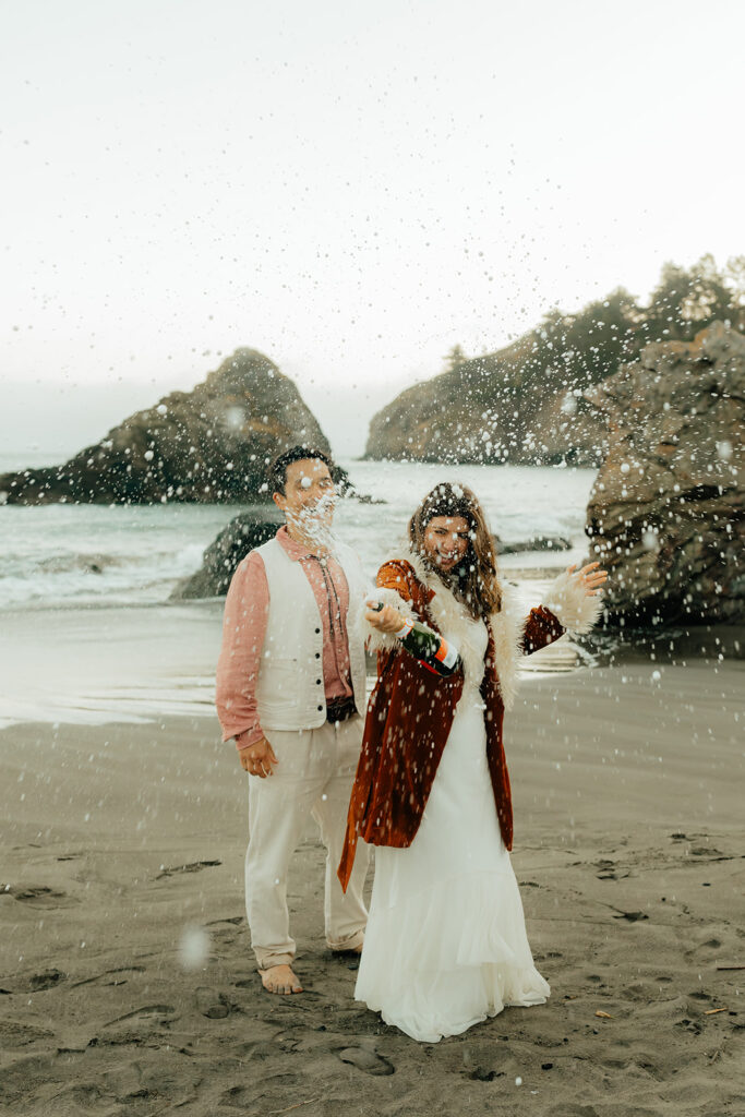 Bride and groom popping champagne on the beach