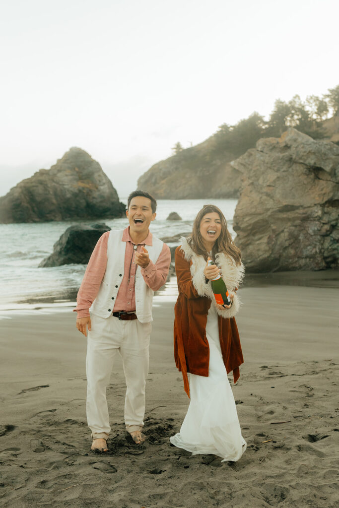 Bride and groom popping champagne on the beach