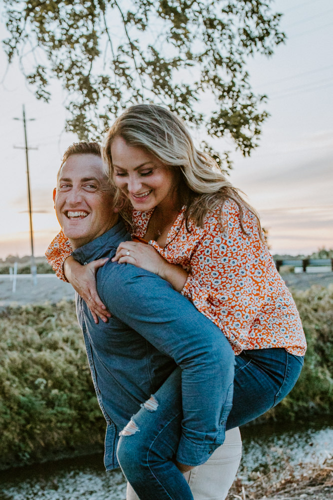 Sacramento River Engagement Session Northern California Weiner dog engagement shoot outfit inspo engagement photos with dog couples shoot posing golden hour sacramento river rachel christopherson photography piggy back laughter together
