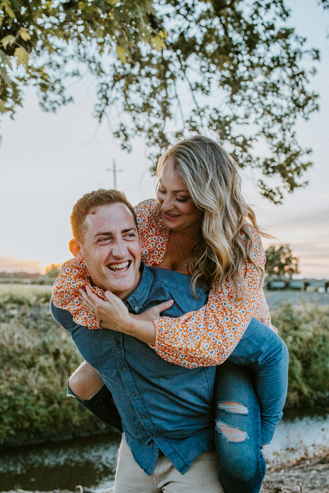 Sacramento River Engagement Session Northern California Weiner dog engagement shoot outfit inspo engagement photos with dog couples shoot posing golden hour sacramento river rachel christopherson photography piggy back happiness