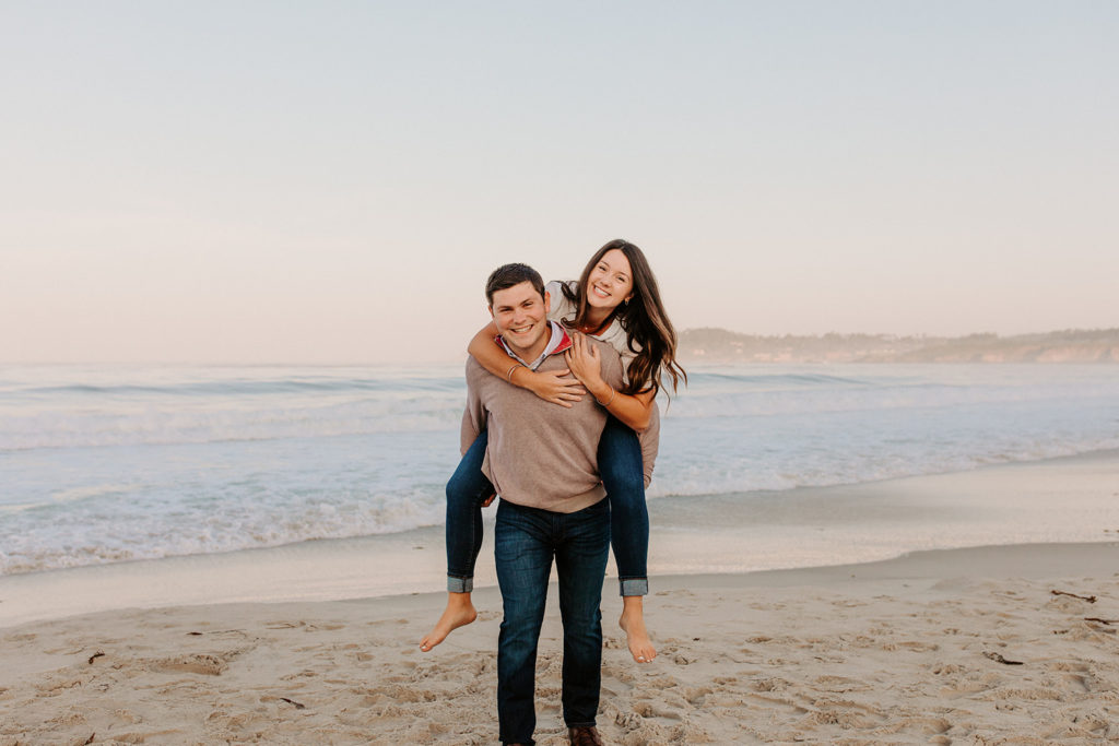 couple on beach piggy back ride, Carmel CA Engagement Photos, Monterey Engagement Photos, Monterey Engagement Photo Locations, Engagement Photo Outfits, California Beach Engagement Photos, Best Locations for Monterey Engagement Photos, What to Wear for Engagement Photos, Rachel Christopherson Photography LLC