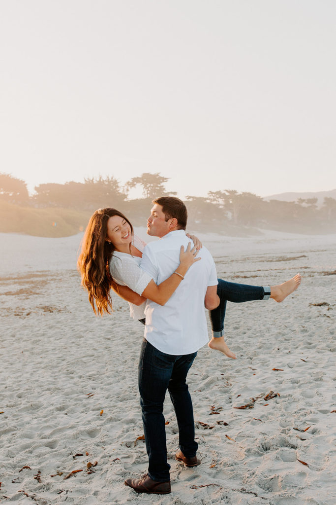 man lifting woman playfully on beach, Carmel CA Engagement Photos, Monterey Engagement Photos, Monterey Engagement Photo Locations, Engagement Photo Outfits, California Beach Engagement Photos, Best Locations for Monterey Engagement Photos, What to Wear for Engagement Photos, Rachel Christopherson Photography LLC