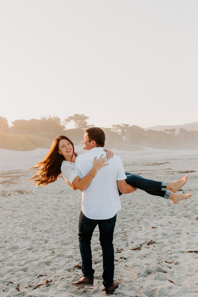 man lifting woman playfully on beach, Carmel CA Engagement Photos, Monterey Engagement Photos, Monterey Engagement Photo Locations, Engagement Photo Outfits, California Beach Engagement Photos, Best Locations for Monterey Engagement Photos, What to Wear for Engagement Photos, Rachel Christopherson Photography LLC