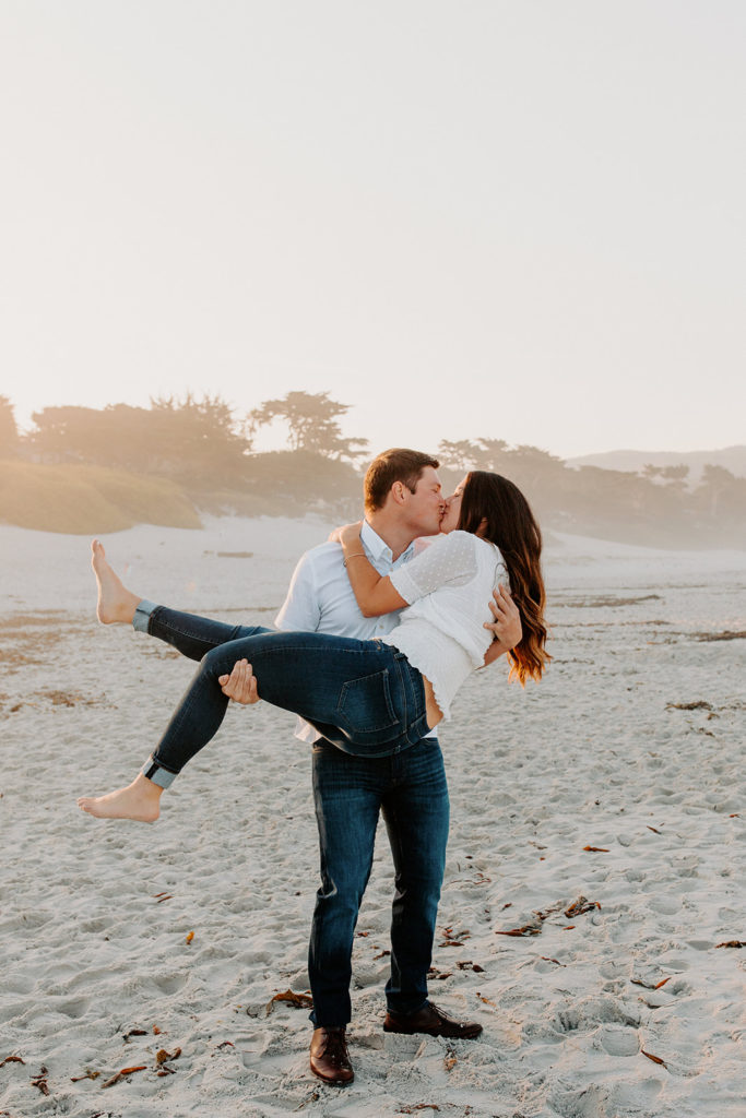 man lifting woman playfully on beach, Carmel CA Engagement Photos, Monterey Engagement Photos, Monterey Engagement Photo Locations, Engagement Photo Outfits, California Beach Engagement Photos, Best Locations for Monterey Engagement Photos, What to Wear for Engagement Photos, Rachel Christopherson Photography LLC