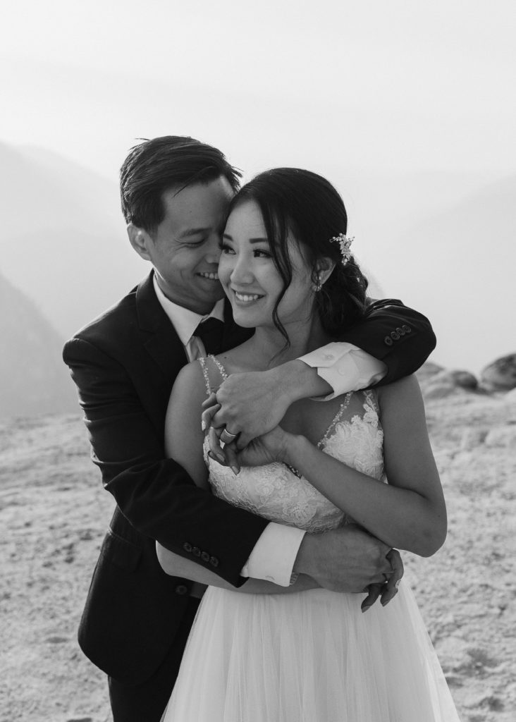 black and white photo of groom arms wrapped around bride from behind, Taft Point elopement, Yosemite Elopement, Glacier Point Elopement, best places to elope in california, northern california elopement, Rachel Christopherson Photography