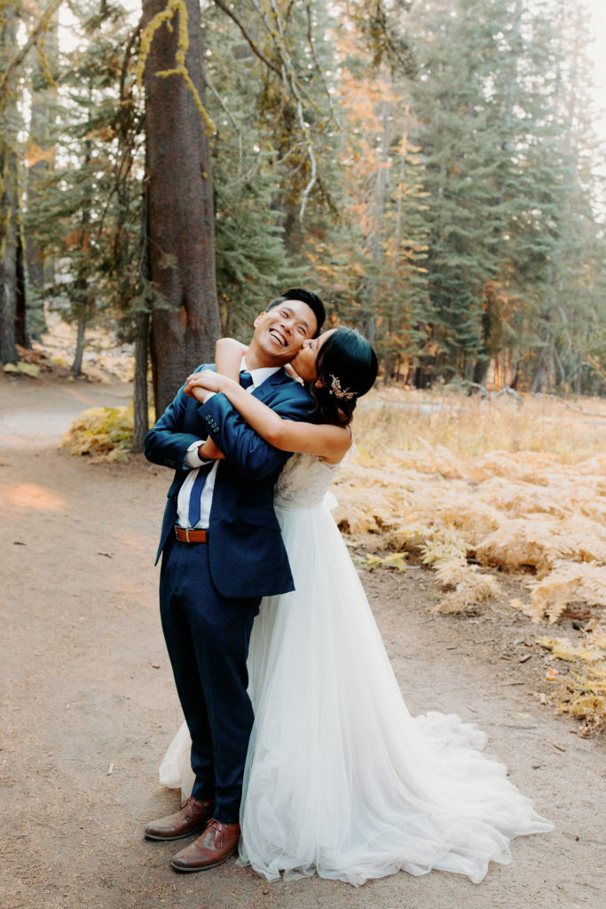 bride hugs groom from behind in forest, adventurous bride, wedding dress and hiking boots, Taft Point elopement, Yosemite Elopement, Glacier Point Elopement, best places to elope in california, northern california elopement, Rachel Christopherson Photography