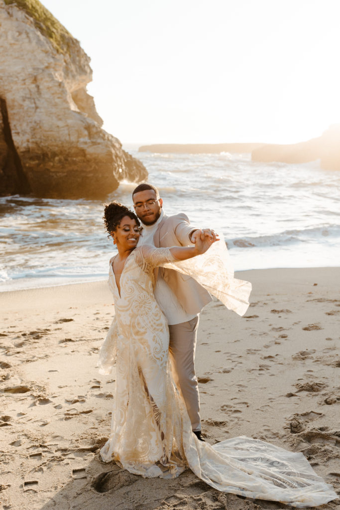 groom hugging bride from behind while swaying dress sleeves, Santa cruz wedding, santa cruz elopement, santa cruz wedding photographer, santa cruz elopement photographer, big sur elopement, boho beach bride, california boho elopement, boho wedding dress, best places to elope in California, California elopement, California beach elopement, boho bride inspo, Rachel Christopherson Photography