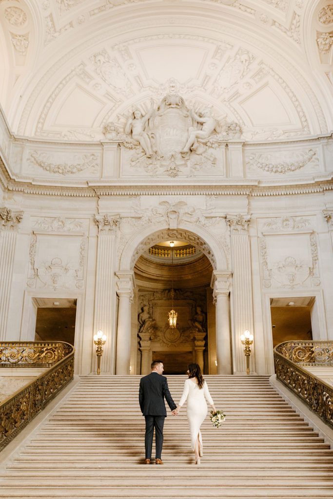 Rachel Christopherson Photographer-SF, San Francisco city hall elopement, san francisco wedding, bride and groom walking upstairs, candid wedding portrait, ivory wedding dress, gray grooms suit