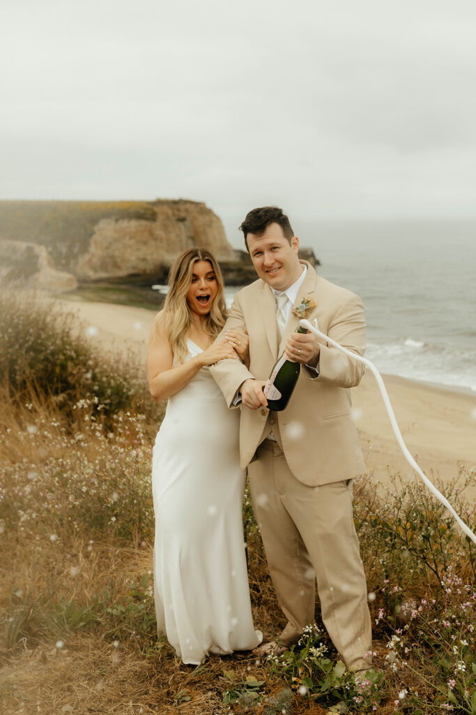 Bride and groom popping champagne on the beach
