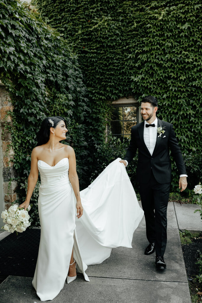 Clos LaChance Wedding - Bride and groom holding hands walking with next to vine covered bricks