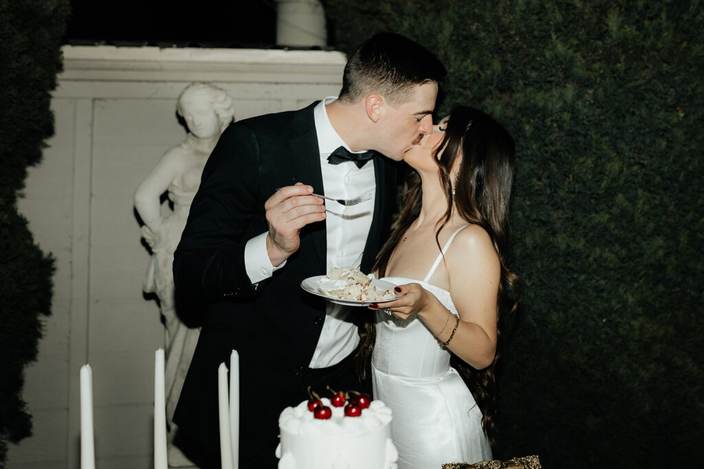 wedding chic couple kissing during cake cutting vintage white cake with cherries on top